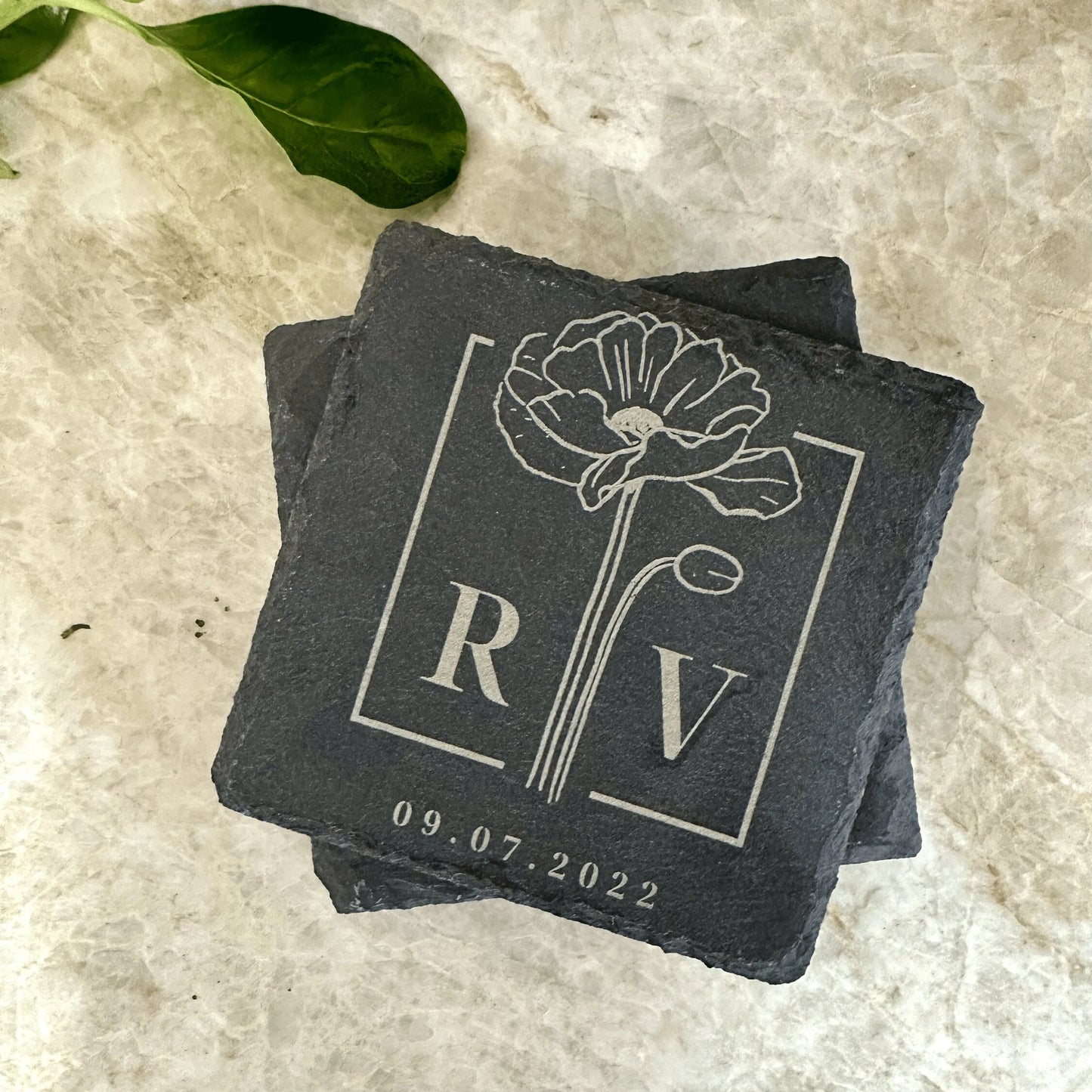 A set of four engraved slate coasters with a natural textured surface, featuring intricate custom designs and text. The coasters have a square shape with beveled edges and protective foam pads on the underside to prevent scratching. They are arranged neatly on a wooden table, showcasing their durable and elegant craftsmanship, perfect for adding a stylish touch to home décor or gifting.